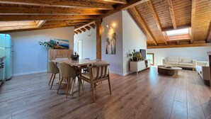 A spacious loft with a high ceiling, wooden beams, a dining area with a table and chairs, a living area with a sofa, and a kitchen with a refrigerator. - C26A01 Apto Moderno en Tagle (Tagle)