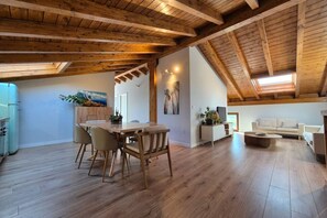 A spacious loft with a high ceiling, wooden beams, a dining area with a table and chairs, a living area with a sofa, and a kitchen with a refrigerator. - C26A01 Apto Moderno en Tagle (Tagle)