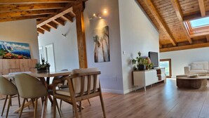 A spacious living area with a wooden ceiling, a dining table with chairs, a sofa, a TV, and a painting on the wall. - C26A01 Apto Moderno en Tagle (Tagle)