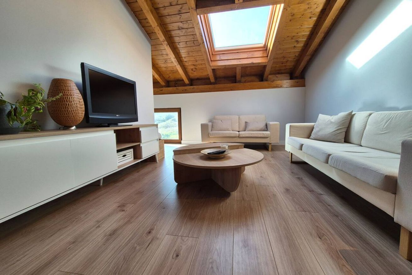 Una sala moderna con techo de madera, televisor de pantalla plana, una mesita redonda y un sofá color beige.
