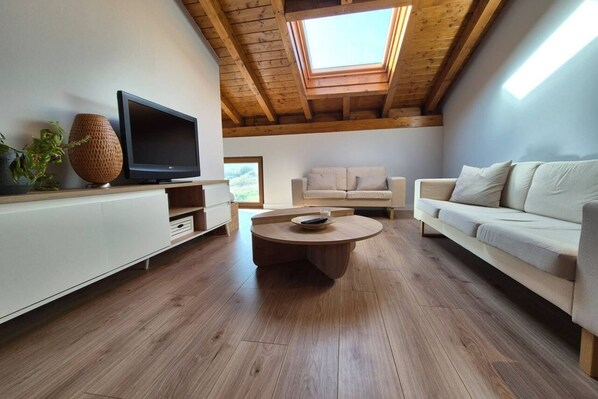 A modern living room with a wooden ceiling, a flat-screen TV, a round coffee table, and a beige sofa.