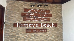A sign for Himeyn Beach Inn Maldives with a logo featuring a sun, waves, and a palm tree.