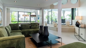 Een moderne woonkamer met een groene bank, een zwarte salontafel en grote ramen met uitzicht op groen buiten.