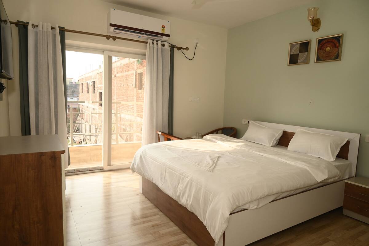 A bedroom with a bed, a wooden nightstand, a desk, and a window with curtains.