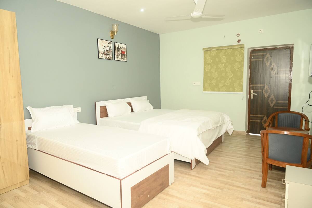 A room with two beds, a wooden chair, a desk, and a door.