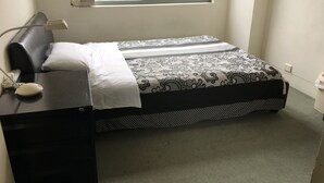 A neatly made bed with a patterned bedspread, a bedside table with a lamp, and a view of buildings through a window. - Sydney City Extra Large furnished Apartment  (Haymarket)