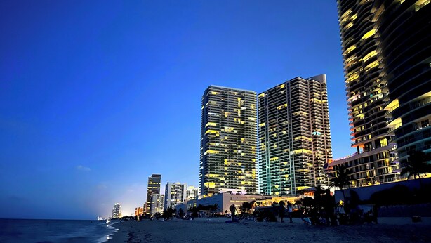 Vistes a la platja amb edificis alts i balcons, sorra i l'oceà al fons.