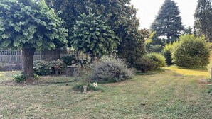 Un jardin agrémenté de divers arbres et arbustes, une clôture blanche et une petite construction.