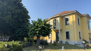 Un bâtiment jaune avec un toit rouge, un grand arbre devant et un petit jardin.