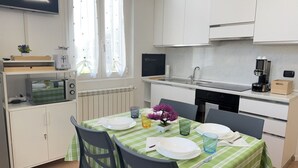 Une cuisine compacte avec des meubles blancs, une table à manger dressée avec des assiettes et des verres, une machine à café et une petite plante posée sur le comptoir.