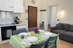 A dining area with a table set for four, a coffee machine, and a sofa in the background.