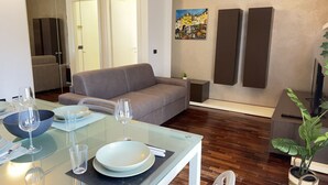 Ein modernes Wohnzimmer mit einem Glastisch, gedeckt für zwei Personen, einem grauen Sofa und einem Gemälde an der Wand.