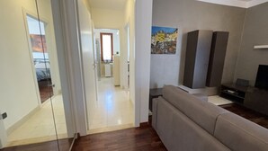 Ein offenes Durchgang führt zu einem Flur, einem Wohnbereich mit Sofa, einem Gemälde und einem TV-Möbel.