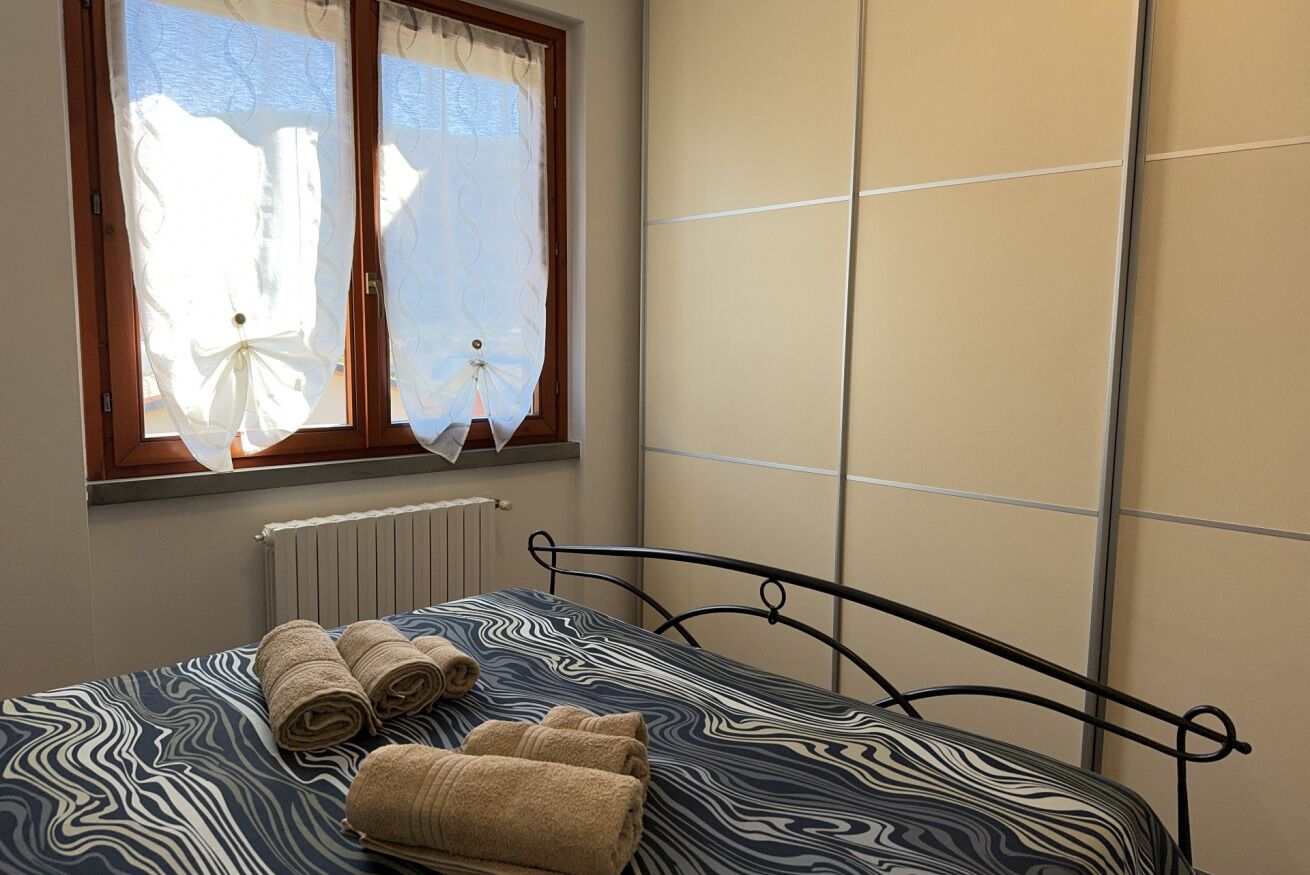 A room with a bed, a window with curtains, a radiator, and a wall with a panel design.