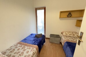 A small room with two beds, a window with curtains, a bedside table, and a shelf with a vase. - 5' from Punta Gro Beach with Free Swimming Pool (Sirmione)