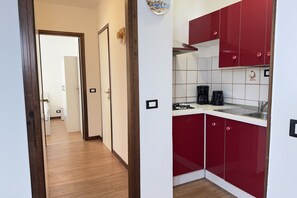A compact kitchen with red cabinets, a coffee maker, and a sink. - 5' from Punta Gro Beach with Free Swimming Pool (Sirmione)