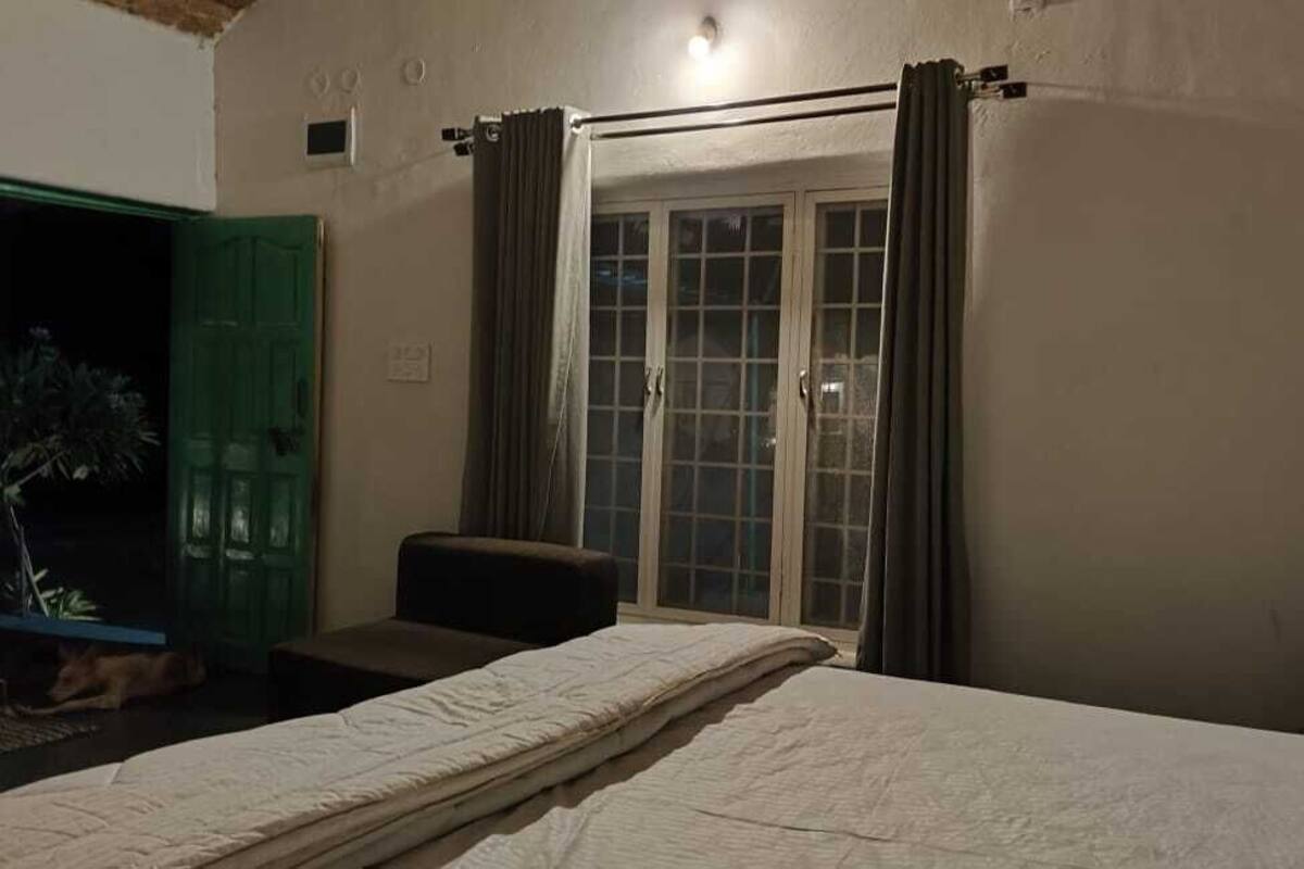 A bedroom with a bed, a chair, a green door, and a window with curtains.