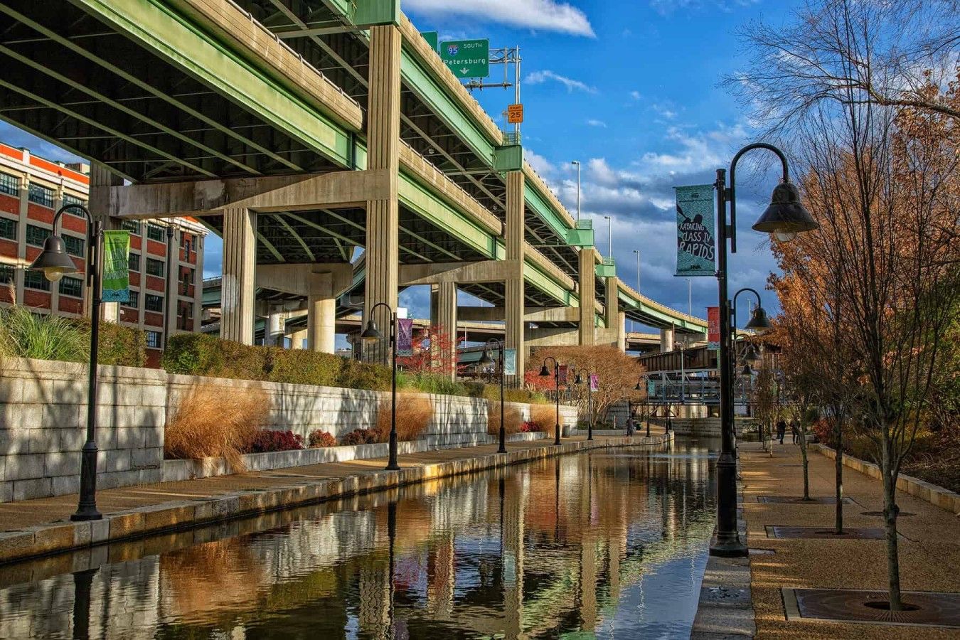 Une structure complexe à plusieurs niveaux, comprenant un pont et une fontaine en premier plan, le tout entouré de verdure et de bâtiments urbains.