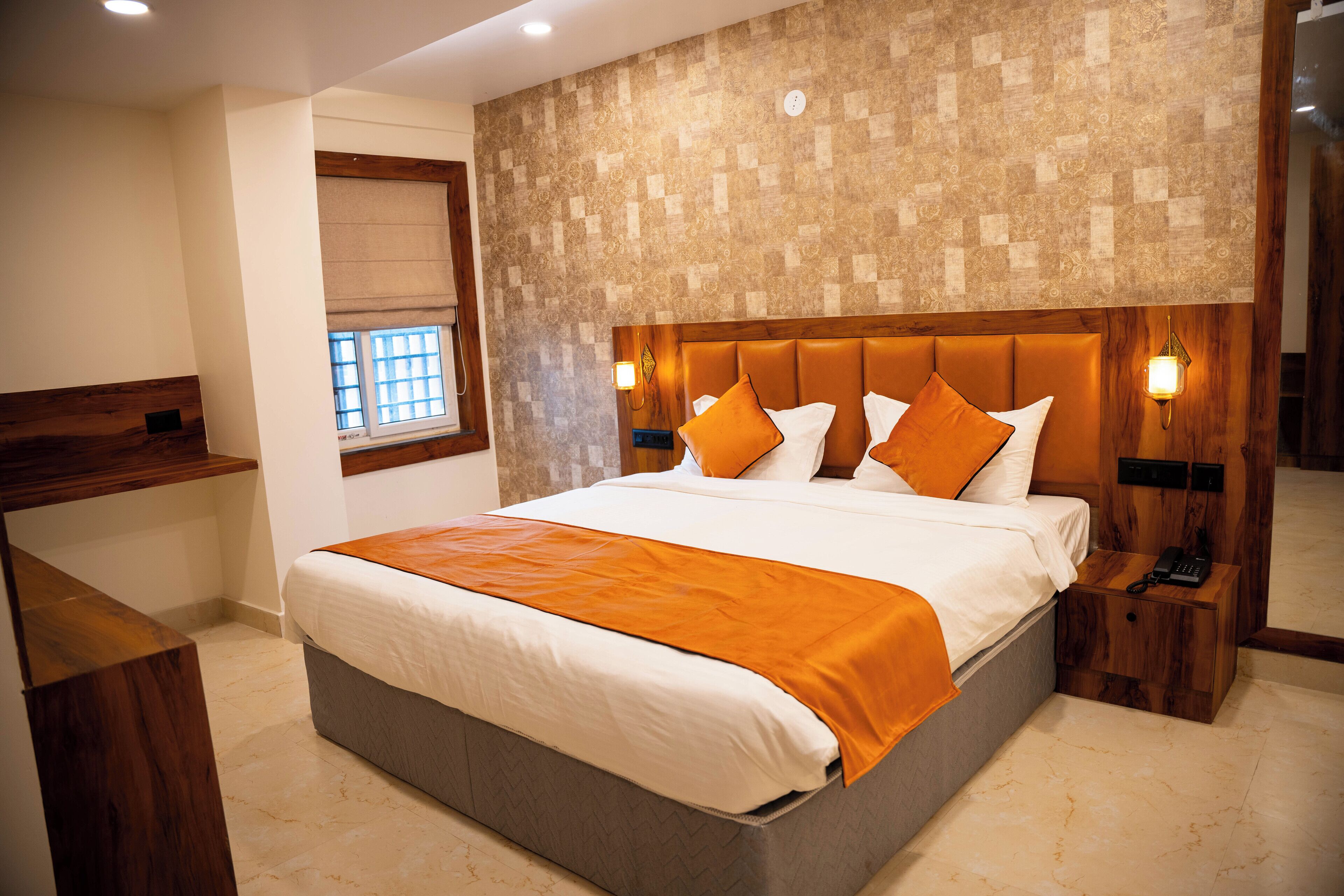 A modern hotel room with a large bed, wooden headboard, and a small bedside table with a phone.