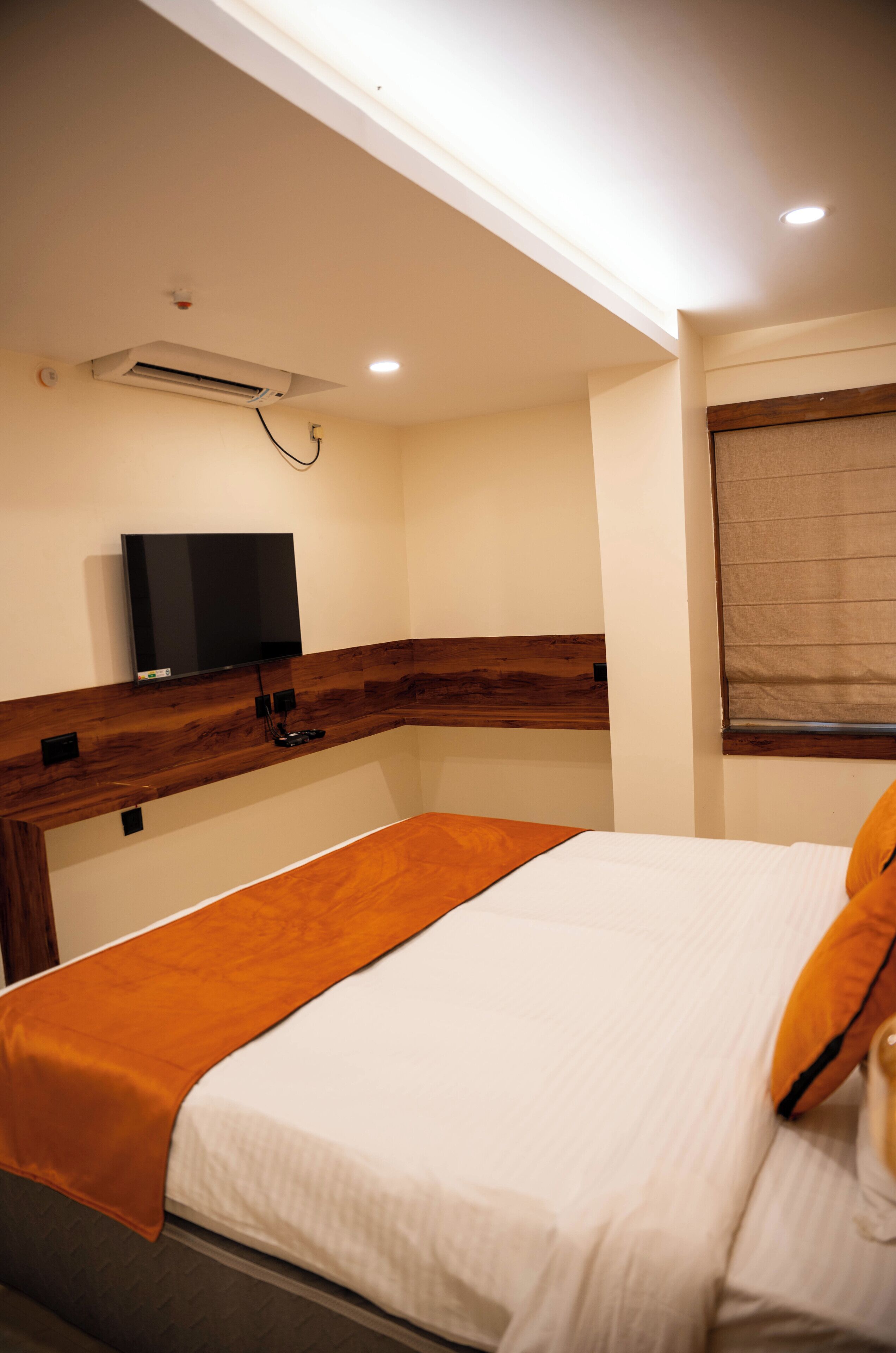 A hotel room with a bed, a television mounted on the wall, and a window with blinds.