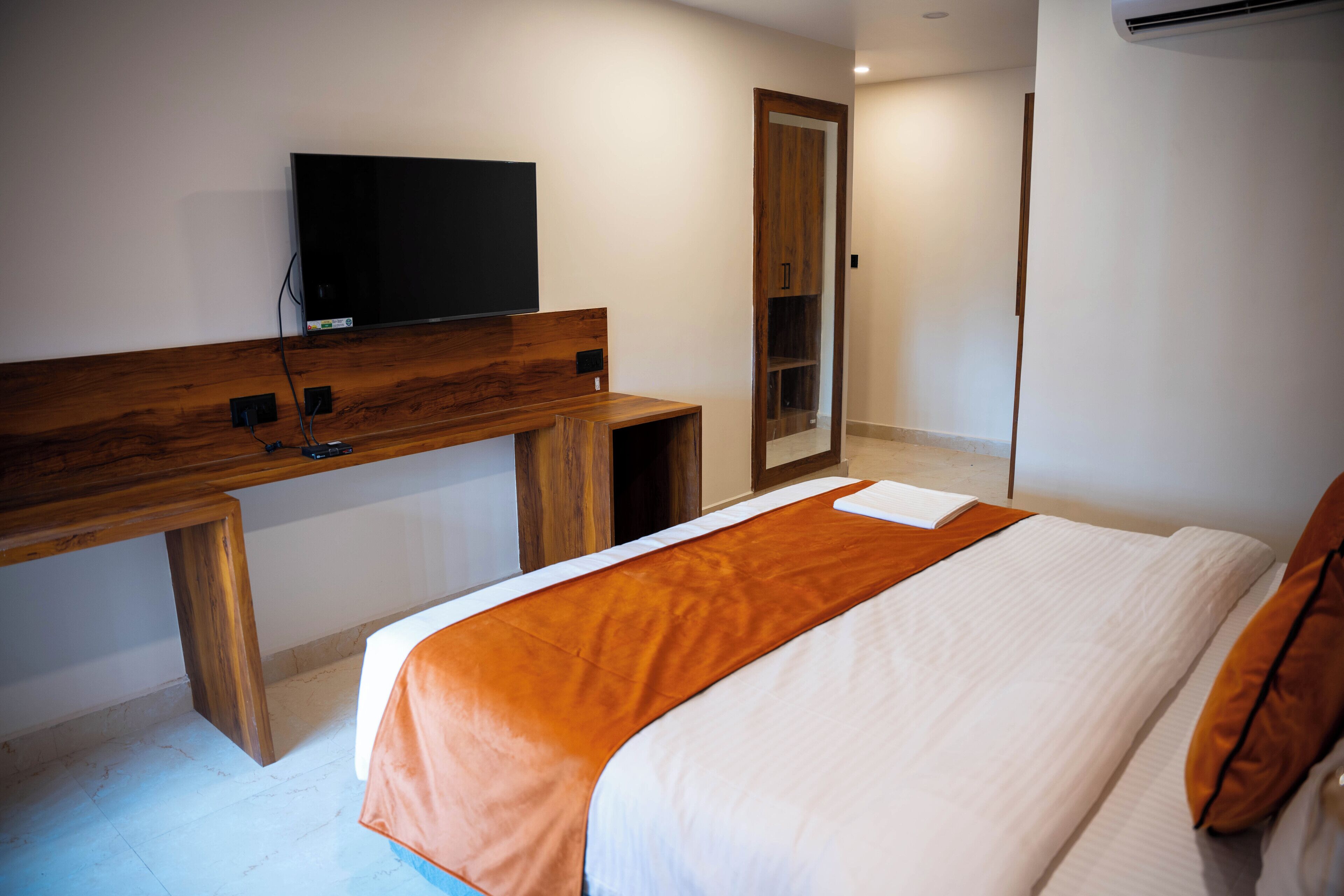 A hotel room with a bed, a wooden desk, a television, and a wardrobe.