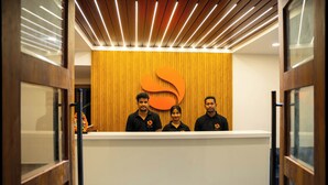 A reception desk with a wooden panel backdrop and a large orange logo. - Hotel Orange (Bhubaneshwar)