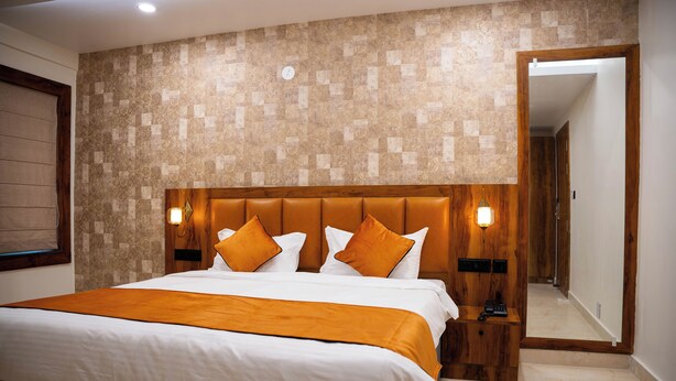 A hotel room with a large bed, wooden headboard, and a patterned wall. - Hotel Orange (Bhubaneshwar)