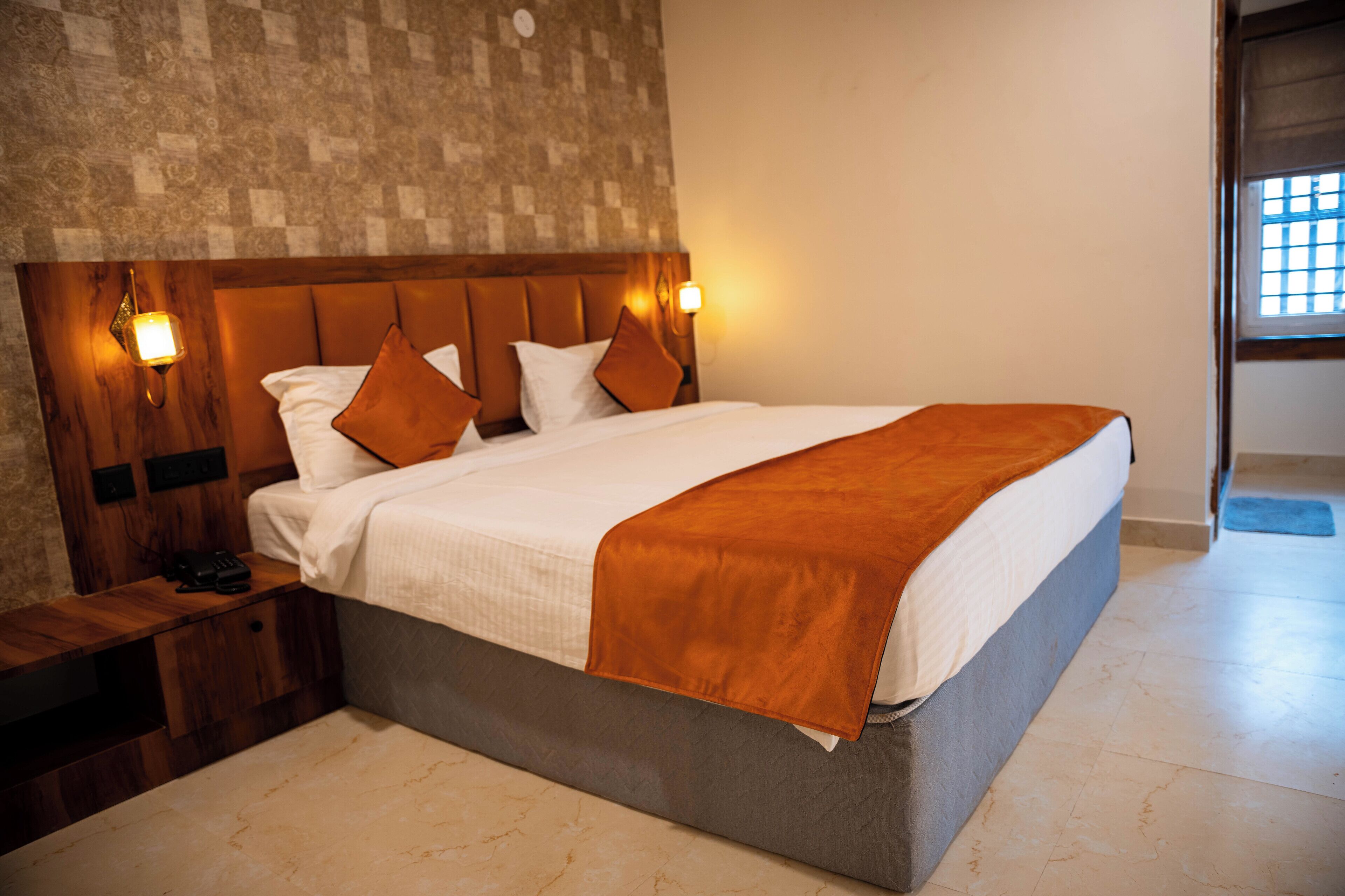 A neatly made bed with a wooden headboard, two bedside lamps, and a brown throw blanket.