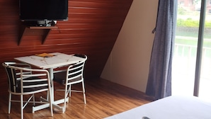 Ett rum med en säng, en tv som är monterad på väggen, ett bord med stolar och ett fönster med gardiner.