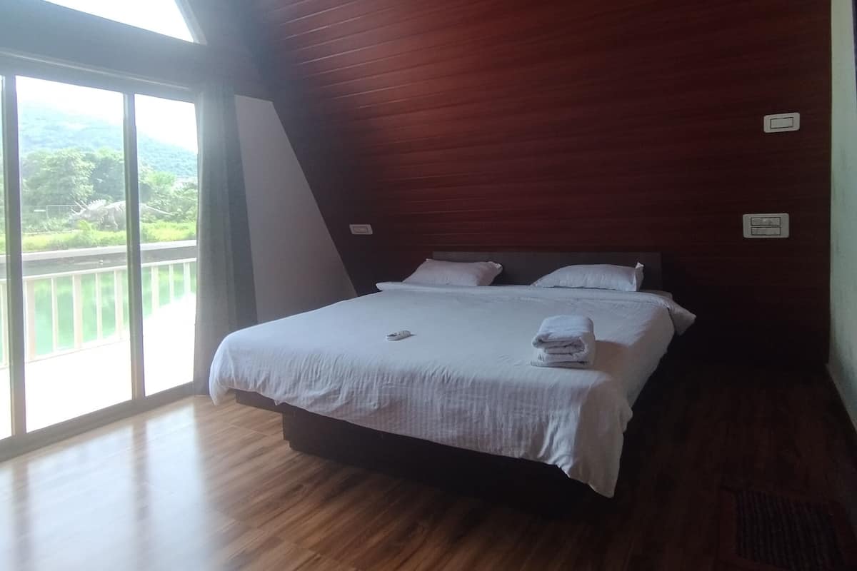A bedroom with a large bed, wooden flooring, and a skylight.