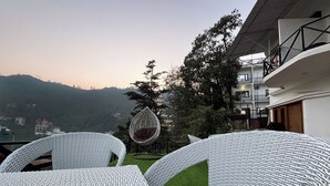 A modern outdoor seating area with white wicker furniture and a hanging chair, overlooking a mountainous landscape. - Hotel Wraveler Inn Mussorrie (Dehradun)