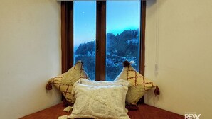 A room with a window overlooking a mountainous landscape. There are two pillows and a blanket on a wooden bench. - Hotel Wraveler Inn Mussorrie (Dehradun)