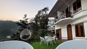 A terrace with wicker furniture, a hanging chair, and a view of a mountainous landscape. - Hotel Wraveler Inn Mussorrie (Dehradun)