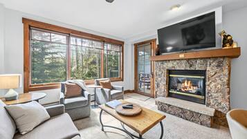 A living room with a fireplace, a television, and large windows.