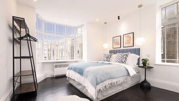 A bedroom with a bed, a radiator, a hanging chair, and a window with a view of buildings.