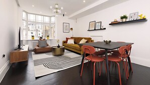 A modern living room with a sofa, a dining table with chairs, a black and white rug, and a large window with city views.