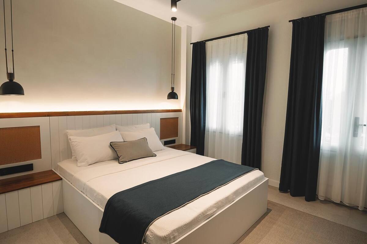 A modern hotel room with a large bed, bedside tables, a wall-mounted heater, and a window with curtains.