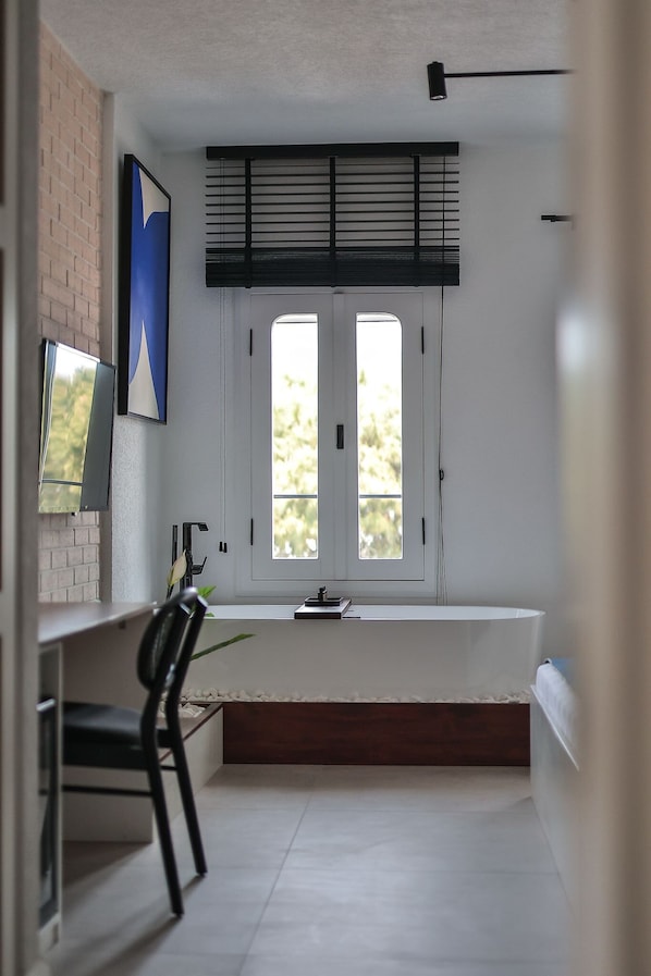 Une pièce moderne avec un mur blanc, une grande fenêtre avec des stores, un bureau avec une chaise et une petite plante.