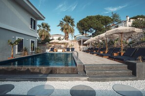 A swimming pool with lounge chairs and umbrellas, surrounded by stone walls and palm trees. - The North Wind  (Ayvalik)
