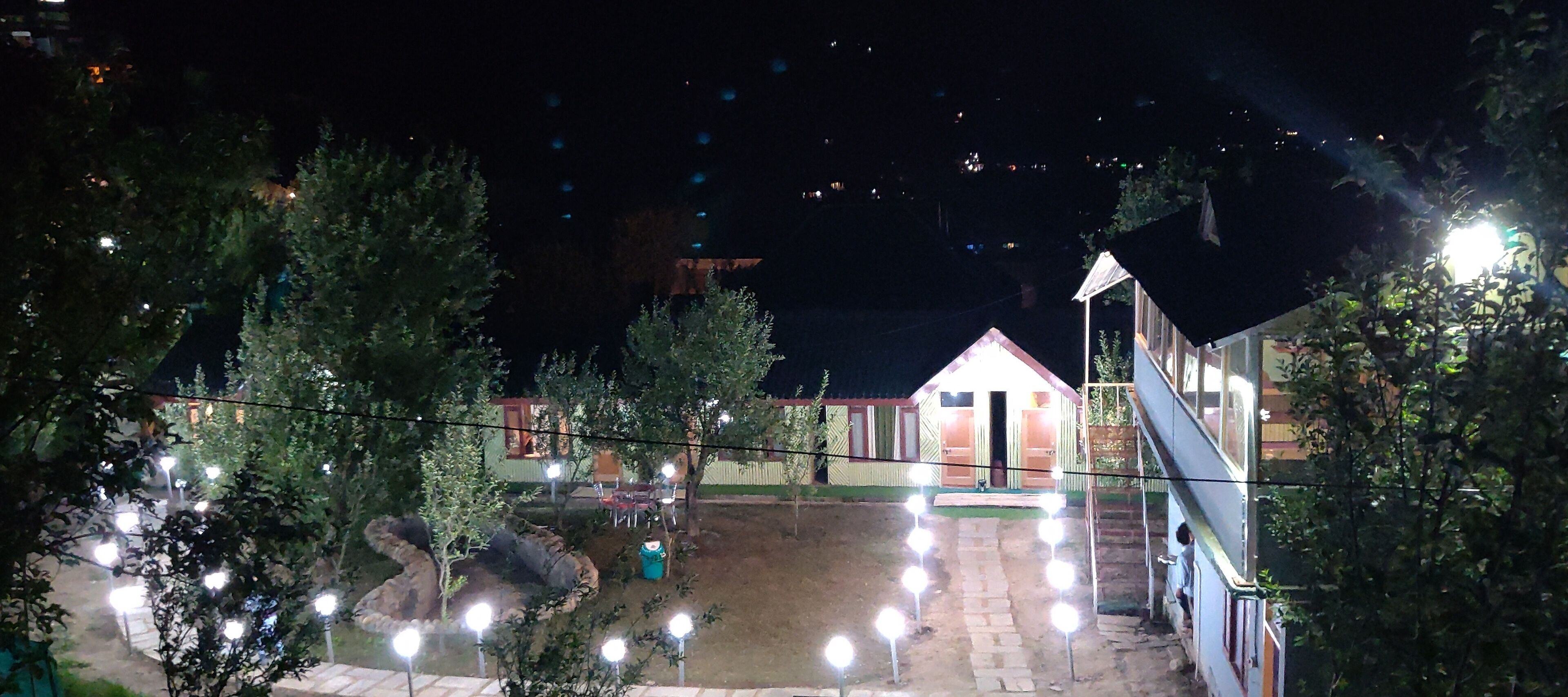 A courtyard with a small building, surrounded by trees and illuminated by string lights.