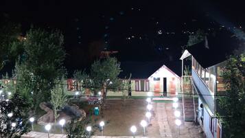 A courtyard with a small building, surrounded by trees and illuminated by string lights.