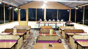 Un restaurant avec des banquettes et des tables, de grandes fenêtres et un plafond haut.