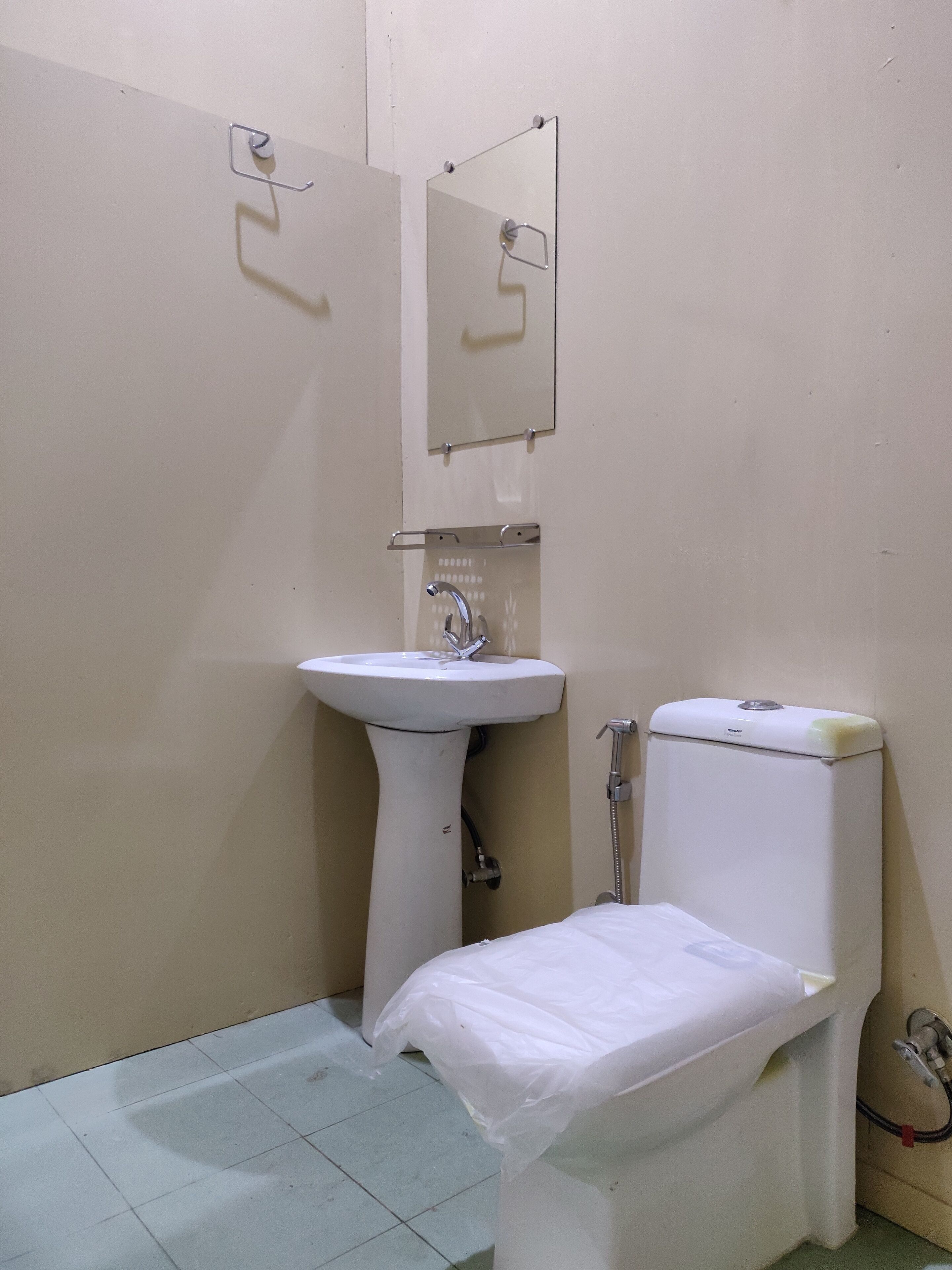 Een kleine, eenvoudige badkamer met een wastafel op voetstuk, een toilet en een spiegel.