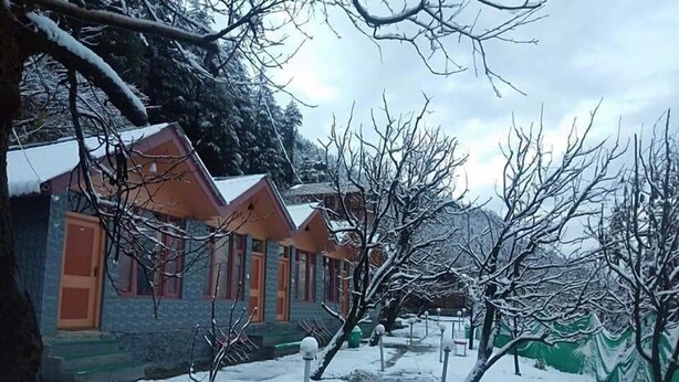 Une rangée de cabanes aux toits inclinés, entourées d’arbres couverts de neige et sous un ciel nuageux.