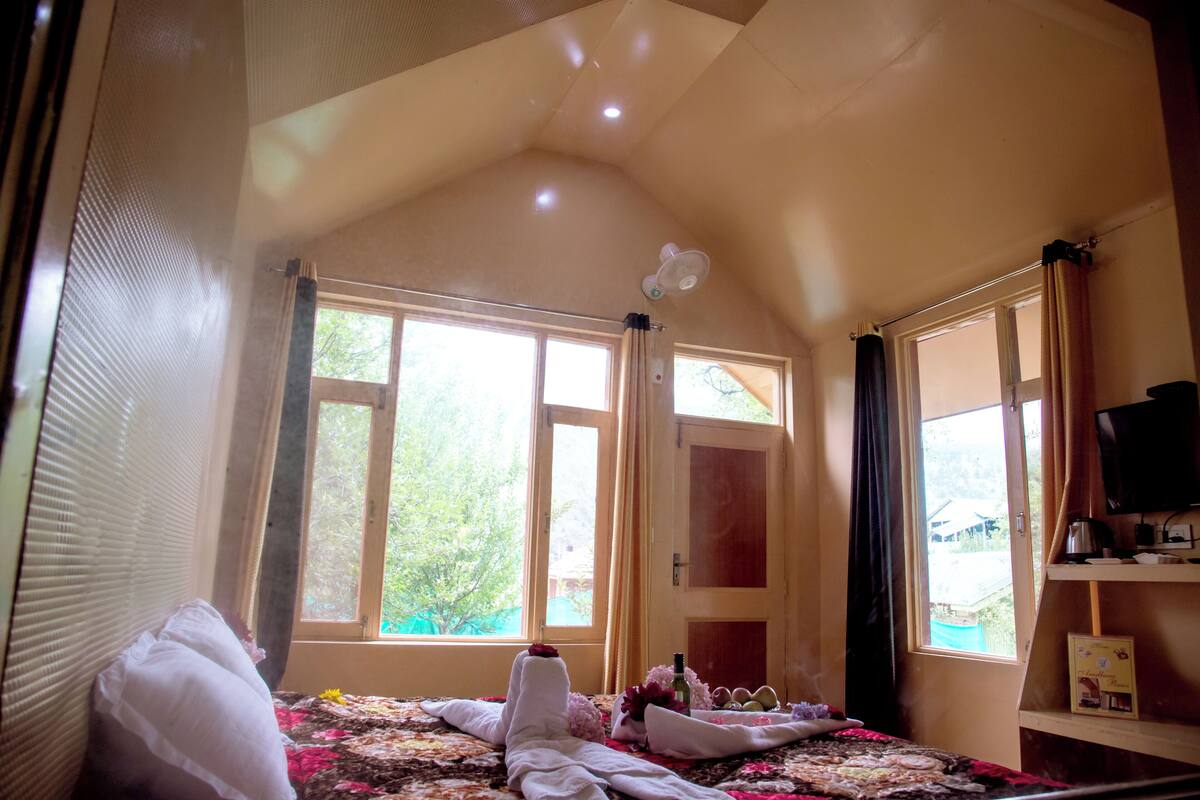 A bedroom with a bed, a window, a fan, and a television on a shelf.