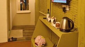 Un espace d’accueil comprenant un téléviseur diffusant une émission, un miroir, une petite table avec une bouteille, une bouilloire et un objet décoratif.