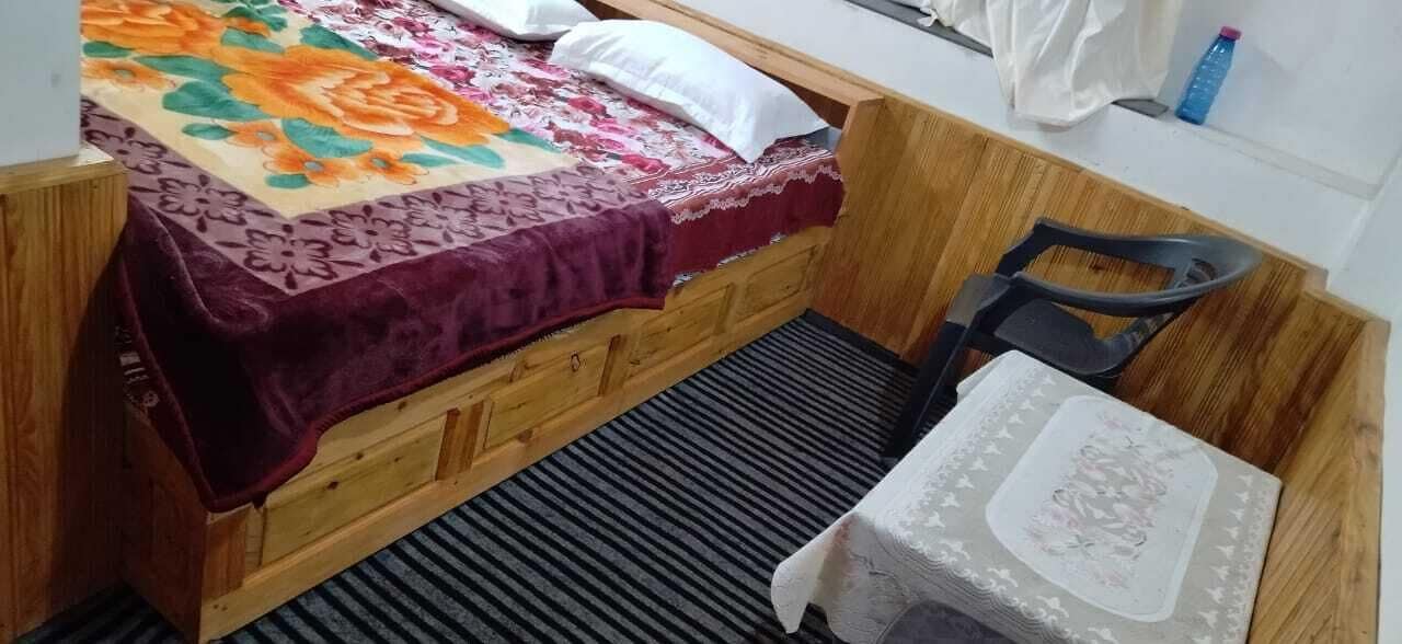 Ein kleines, gemütliches Zimmer mit einem Einzelbett, einem Holz-Kopfteil, einem Tisch mit Tischdecke und einem Stuhl.