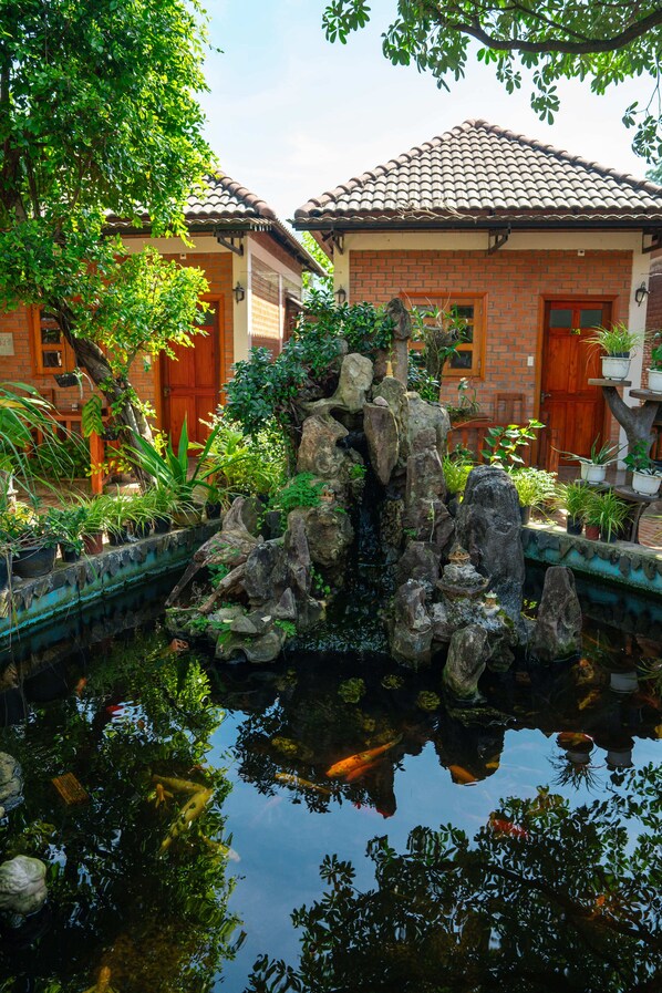 A traditional brick building with a tiled roof, a small pond with rocks and plants, and a wooden door. - Duy Ngoc Resort Phu Quoc (Phu Quoc)
