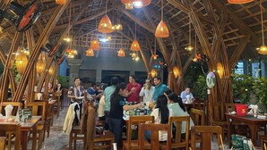 An indoor dining area with bamboo ceiling structures and hanging light fixtures. Tables are set with chairs, and people are seated and standing. - Duy Ngoc Resort Phu Quoc (Phu Quoc)
