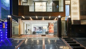 Entrada d'un hotel de disseny modern, amb una porta de vidre, una estàtua de Buda i un rètol que indica 'Suite Grand Plaza Noida'.